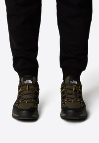 Ciemnoszare buty trekkingowe z czarnymi akcentami, żółtymi sznurowadłami i strukturalnymi panelami z siateczki. Posiadają wyścieloną podeszwę i wzmocniony czubek.