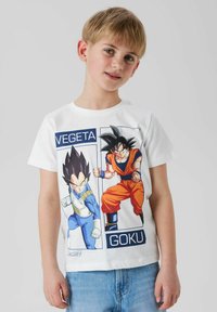 Garçon portant un t-shirt blanc avec Vegeta en armure bleue et Goku en tenue orange de Dragon Ball Z, associé à un jean bleu clair.