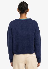 Marinblå stickad tröja med rund halsringning, oversized passform och ribbad nederkant. Mjuk textur, sänkta axlar och halvlång rygg.