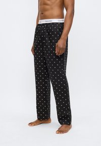 Μαύροι παντελόνες πιτζάμας με μοτίβο λευκού λογότυπου, ελαστική ζώνη μέσης με το όνομα της μάρκας, άνετη εφαρμογή, ελαφρύ ύφασμα και σχεδιασμό με ίσιο πόδι.