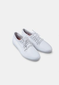 Fehér bőr sportcipők sima felülettel, kerek orral, hagyományos fűzős kialakítással és gumitalppal a tapadás érdekében.