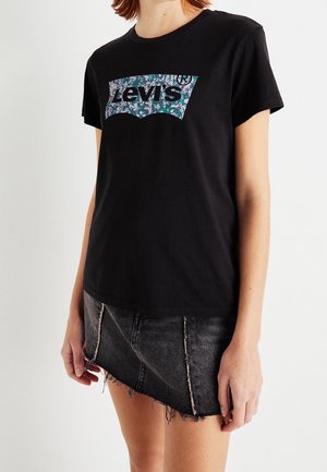Person wearing a black Levi's t-shirt with a floral logo and a black asymmetrical denim mini skirt with frayed edges.
