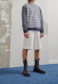 Sudadera con rayas horizontales azules y blancas, combinada con pantalones cortos blancos y botas de cuero negro hasta el tobillo. Textura suave, corte relajado.