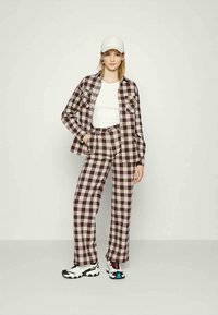 Conjunto xadrez em tons de castanho e creme, com uma camisa oversized e calças largas, combinado com ténis brancos e um boné branco.