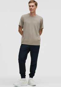 Beige rövidujjú póló, laza fazonban, sötétkék joggers-nadrággal, amely rugalmas szegélyekkel és oldalzsebekkel rendelkezik. Fehér sportcipőkből áll a szett.