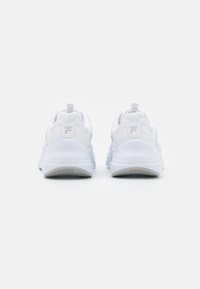 Chaussures de sport blanches avec une tige en tissu texturé, un col rembourré et un talon renforcé avec une languette de traction. Semelle extérieure en caoutchouc avec un motif en zigzag.