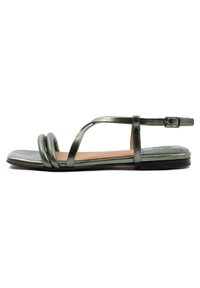 Grüne metallische flache Sandalen mit einer abgerundeten Zehenpartie, die ein Kreuzriemen-Design und zwei gedrehte Riemen vorne haben. Schnallenverschluss am Knöchel.