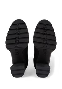 Czarne botki sięgające kostki z fakturowaną gumową podeszwą, z żłobionym wzorem i wytłoczonym napisem "CALVIN KLEIN JEANS" na spodzie. Gładki materiał wierzchni.