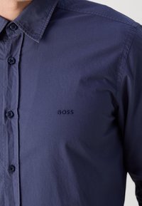 Marinblå skjorta med knappar i slät tyg, med klassisk krage, broderad logotyp och kontrasterande knappar.