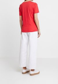 Rød kortærmet T-shirt med rund halsudskæring, parret med hvide brede bukser og hvide sneakers med en naturlig platformssål.