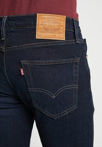 Jeans Levi's blu scuro con tasca posteriore e cuciture caratteristiche, etichetta in pelle marrone Levi Strauss & Co. sulla vita.