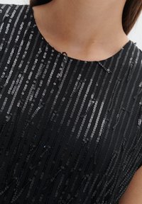 Černé šaty s texturovaným vzorem svislých linií z flitrů. Kulatý výstřih, krátké rukávy a hladký povrch látky.