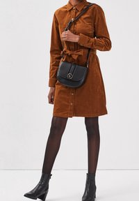 Hnědá kordurová šatová košile s knoflíkovým zapínáním, opásaným pasem a dvěma náprsními kapsami. V kombinaci s černou crossbody taškou a kotníkovými botami na podpatku.