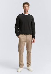 Juodas megztinis, smėlio spalvos kelnės, balti batai. Megztinis turi apvalų kaklą ir ilgomis rankovėmis; kelnės yra tiesaus kirpimo su diržu.