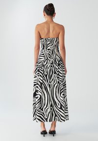 Axelbandslös maxiklänning i svartvitt zebramönster. Tillverkad av lätt tyg, med en figurnära överdel och en veckad kjol.