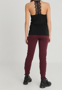 Černý tílko s krajkovým detailem na zádech, které je kombinováno s vínovými přiléhavými kalhotami a černými šněrovacími botami. Hladký materiál s těsným střihem.