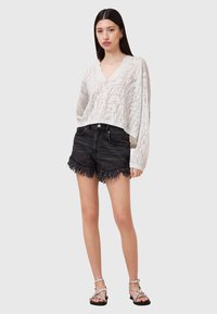 Leichtes, weißes Strickoberteil mit V-Ausschnitt und strukturiertem Muster, kombiniert mit hoch taillierten, ausgefransten schwarzen Denim-Shorts und Riemchensandalen.