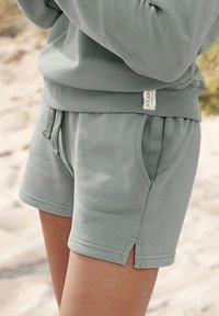 Ljusgröna bomullsshorts med resårmidja, sidofickor och en liten märkesetikett. Tyget har en mjuk textur.