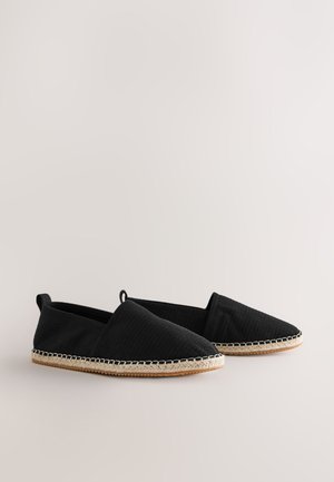 Espadrillas in tessuto nero con superficie strutturata e design senza lacci. Caratterizzate da suola in giunco intrecciato e cuciture chiare a contrasto lungo il bordo.