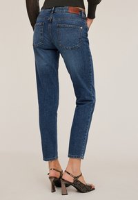 Granatowe dżinsy o prostym kroju, pięć kieszeni, brązowa skórzana naszywka z tyłu. W połączeniu z sandałami na obcasie w wzór węża.