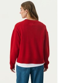 Red knitted sweater with a crew neck, ribbed cuffs, and hem. Features a relaxed fit and a smooth texture, paired with blue jeans.