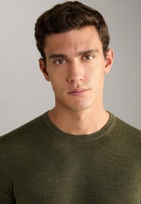 Olive green, crew-neck knitted sweater with a textured fabric. Close-up view emphasizes the smooth surface and ribbed neckline.