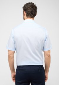 Lichtblauw kortom-shirt met een soepele textuur, een geknoopte kraag en opgerolde mouwen, gecombineerd met donkerblauwe broek.