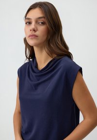 Top senza maniche color blu navy con scollatura a draping, realizzato in tessuto morbido, caratterizzato da una superficie liscia e una vestibilità rilassata.