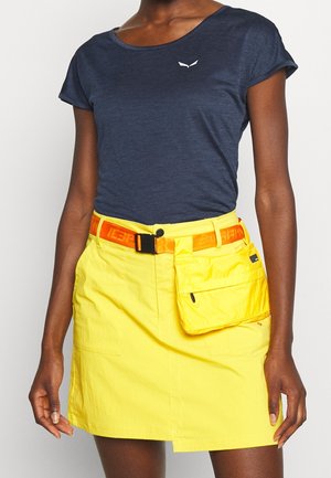 Woman wearing a navy blue short-sleeve top and a bright yellow skirt with an orange belt and attached pouch on the front right side.