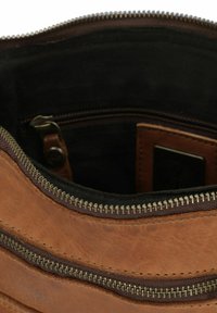 Braune Lederhandtasche mit zwei Reißverschlüssen, ausgestattet mit einer strukturierten Oberfläche und einem schwarzen Innenfutter. Das Innenfutter enthält eine kleine Tasche.