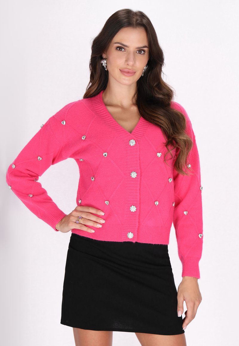 Cardigan tricotat roz cu decolteu în V, model cu diamante, decorat cu strasuri argintii. Design ajustat cu mâneci lungi și închidere cu nasturi.