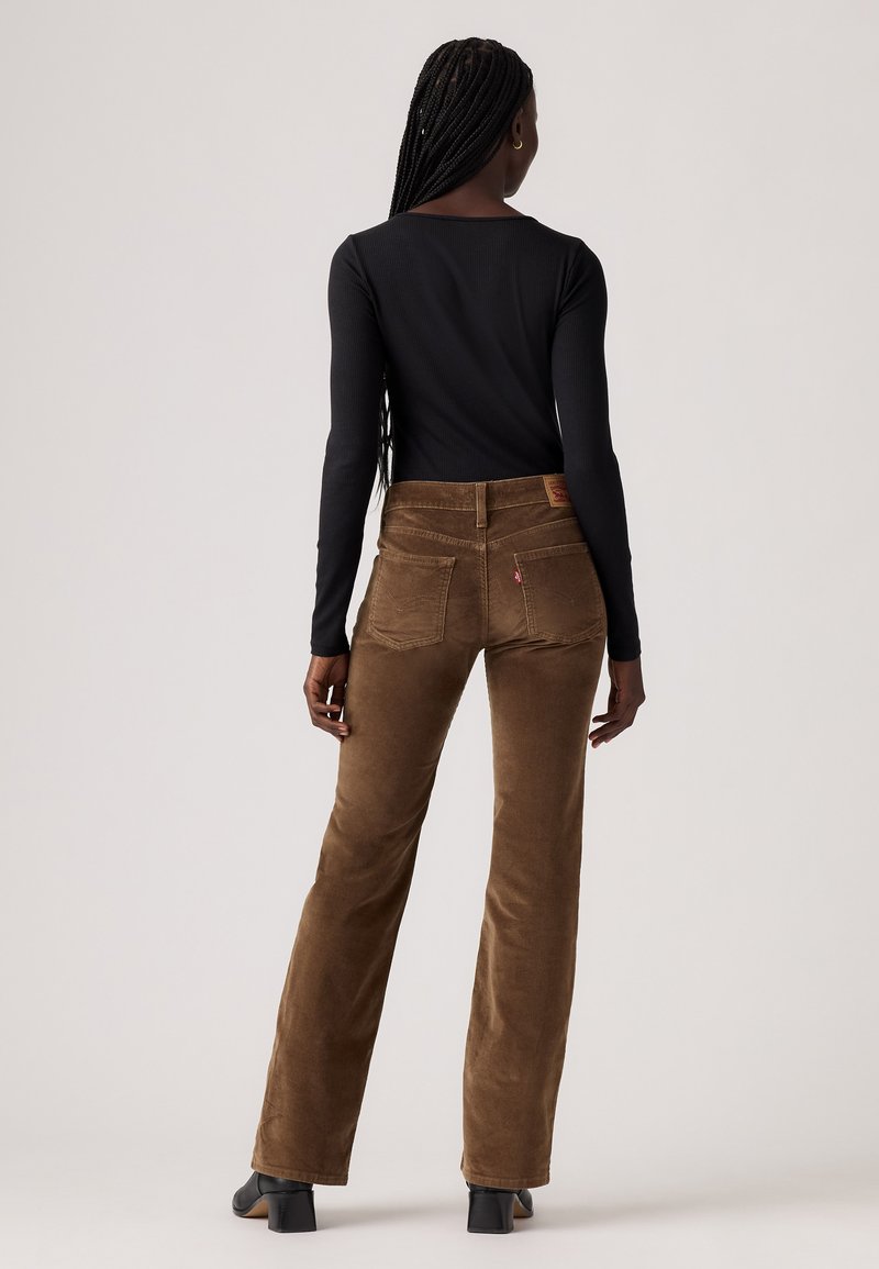 Pantalons évasés en velours côtelé marron avec une taille haute, dotés de poches arrière, d'un patch en cuir et d'une finition texturée. Haut noir à manches longues.