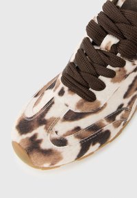 Sneaker con motivo animale marrone e crema, con lacci spessi intrecciati marroni e punta in gomma color marrone chiaro, su sfondo bianco.