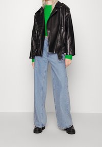 Černá kožená motocyklová bunda, zelený pletený svetr a volné modré džíny. Černé robustní boty dotvářejí celkový vzhled.