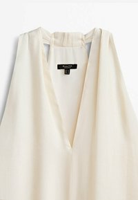 Blouse sans manches couleur crème avec un profond décolleté en V et un tissu doux et léger ; comprend une étiquette avec les informations de taille à l'arrière.