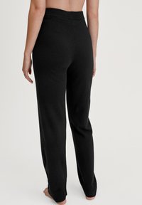 Zwarte gebreide broek met een zachte textuur, voorzien van een brede elastische tailleband en taps toelopende boorden bij de enkels. Geen zichtbare patronen of hardware.