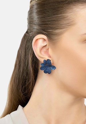 Blauwe bloemenoorbellen met gestructureerde bloemblaadjes, met een multidimensionaal ontwerp. Geplaatst tegen een neutrale huidtint en haarkleur.