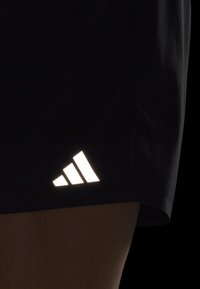 Mustat urheilushortsit, joissa on heijastava valkoinen Adidas-trefoiili-logo alakulmassa. Sileä pinta ja kevyt muotoilu.
