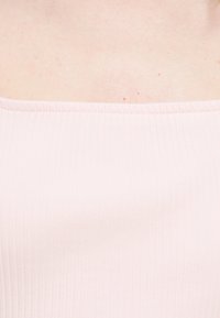 Gros plan sur le haut de la poitrine et les épaules d'une personne portant un haut sans bretelles côtelé rose pâle.