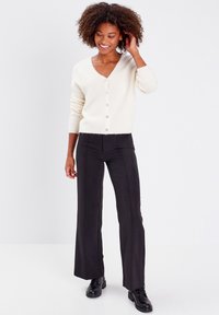 Cardigan blanc à col en V avec une texture douce et cinq boutons, associé à un pantalon noir taille haute et des bottes noires à lacets.