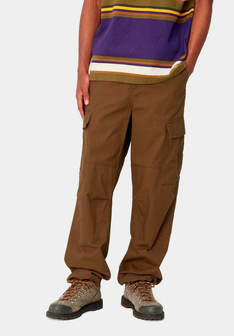 Pantalones cargo marrones con múltiples bolsillos y un ajuste holgado, fabricados con una tela texturizada. Combinados con botas de senderismo grises.
