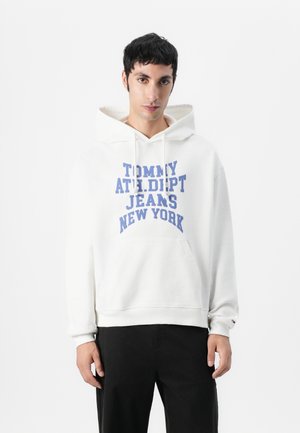 Sweat à capuche blanc avec un grand texte bleu indiquant "TOMMY ATH. DEPT. JEANS NEW YORK." Comprend une poche kangourou à l'avant et un cordon de serrage à la capuche.