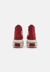 Baskets montantes en toile rouge avec des semelles en caoutchouc blanc. Présente un patch avec le logo étoile sur chaque talon et des coutures contrastées.