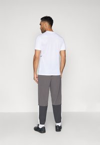 Λευκό αθλητικό μπλουζάκι με κοντά μανίκια και υφή μεσού. Γκρι στενές παντελόνες με μαύρες και λευκές ρίγες στις πλευρές. Μαύρα αθλητικά παπούτσια.