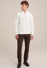 Sudadera blanca con cuello de cremallera y mangas largas, combinada con pantalones ajustados marrones y mocasines negros. Textura suave, diseño minimalista.