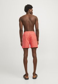 Bañador de coral con cinturilla elástica, bolsillo trasero y logotipo en texto blanco en un lado. Tejido suave con un ajuste relajado.