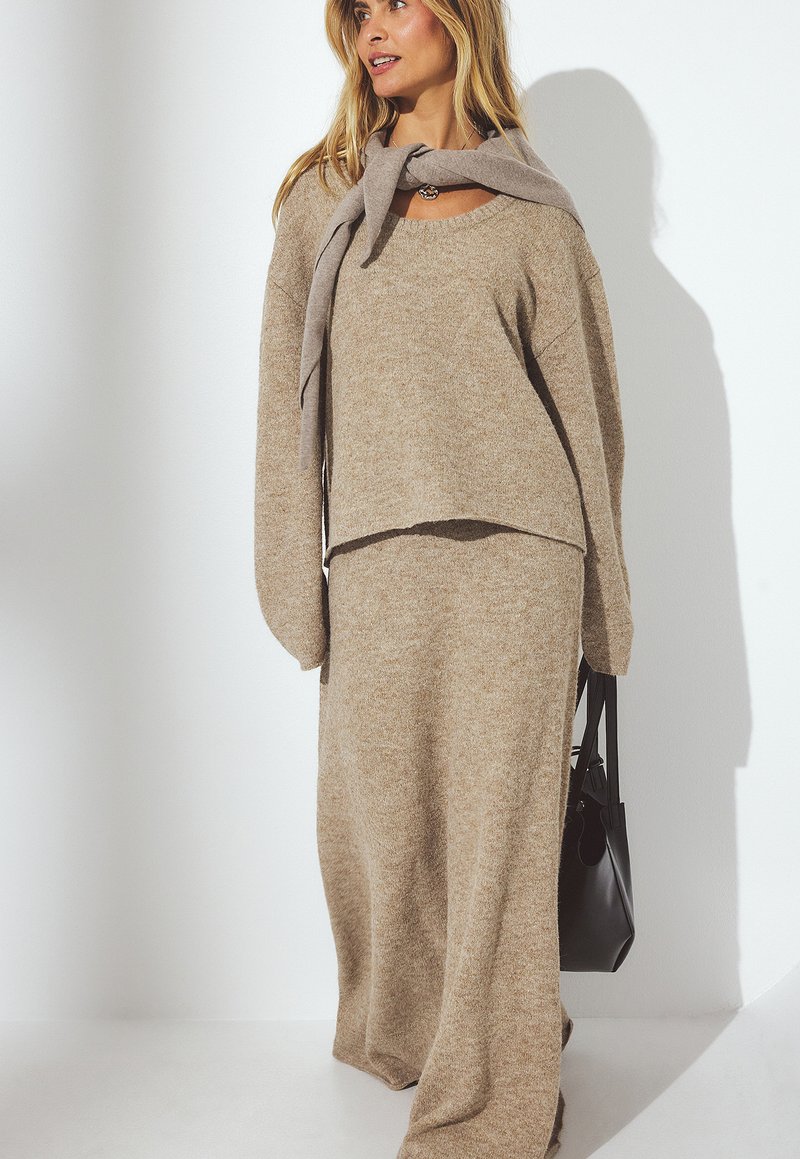 Maglione beige a maglia e gonna maxi coordinata con vestibilità comoda. Il maglione ha un collo a giro e maniche oversize. Borsa a mano nera come accessorio.