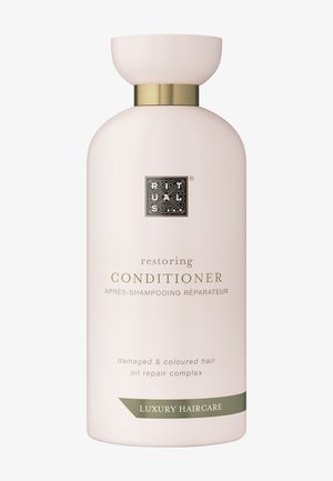 Bouteille de revitalisant, rose pâle, forme ronde, accent doré autour du cou, logo en relief, texte indiquant son adéquation pour les cheveux abîmés et colorés.