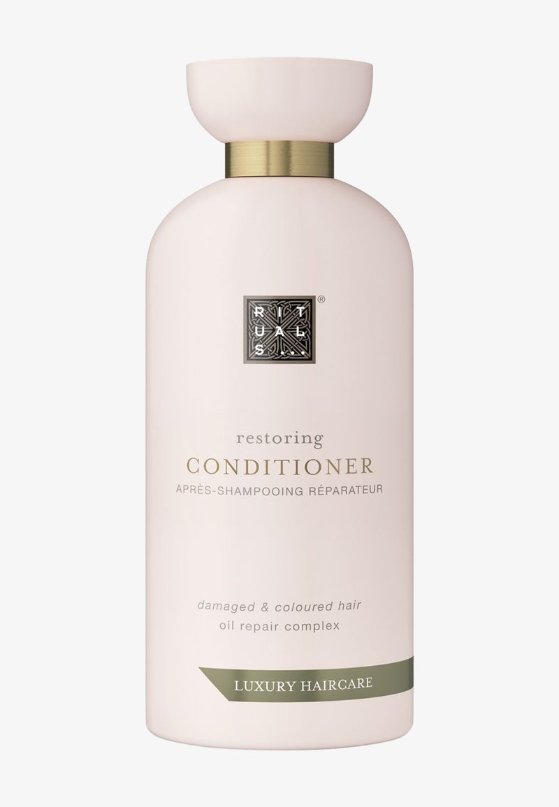 Botella de acondicionador restaurador, color rosa pálido, forma redonda, acento dorado alrededor del cuello, logo emblema, texto que indica su idoneidad para cabello dañado y teñido.