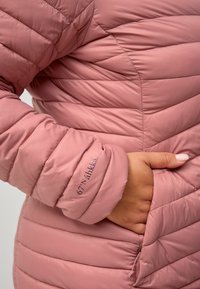 Pink pufferjakke med quiltet design, der har en lynlåslomme og et broderet logo på manchetten. Glat, let skinnende stofstruktur.